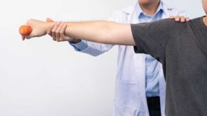 A therapist guides an adult through gentle strengthening exercises in a bright rehabilitation room.
