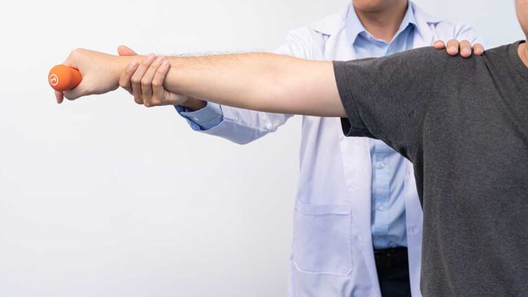 A therapist guides an adult through gentle strengthening exercises in a bright rehabilitation room.