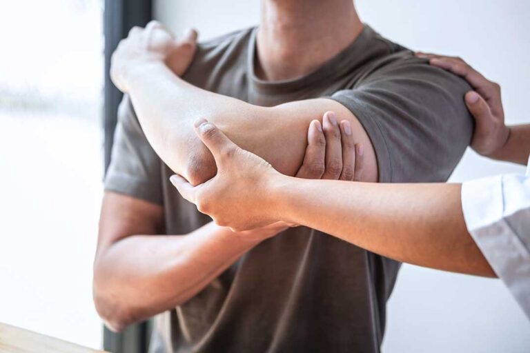 Person elevating a swollen ankle on pillows with a towel-wrapped cold pack nearby.